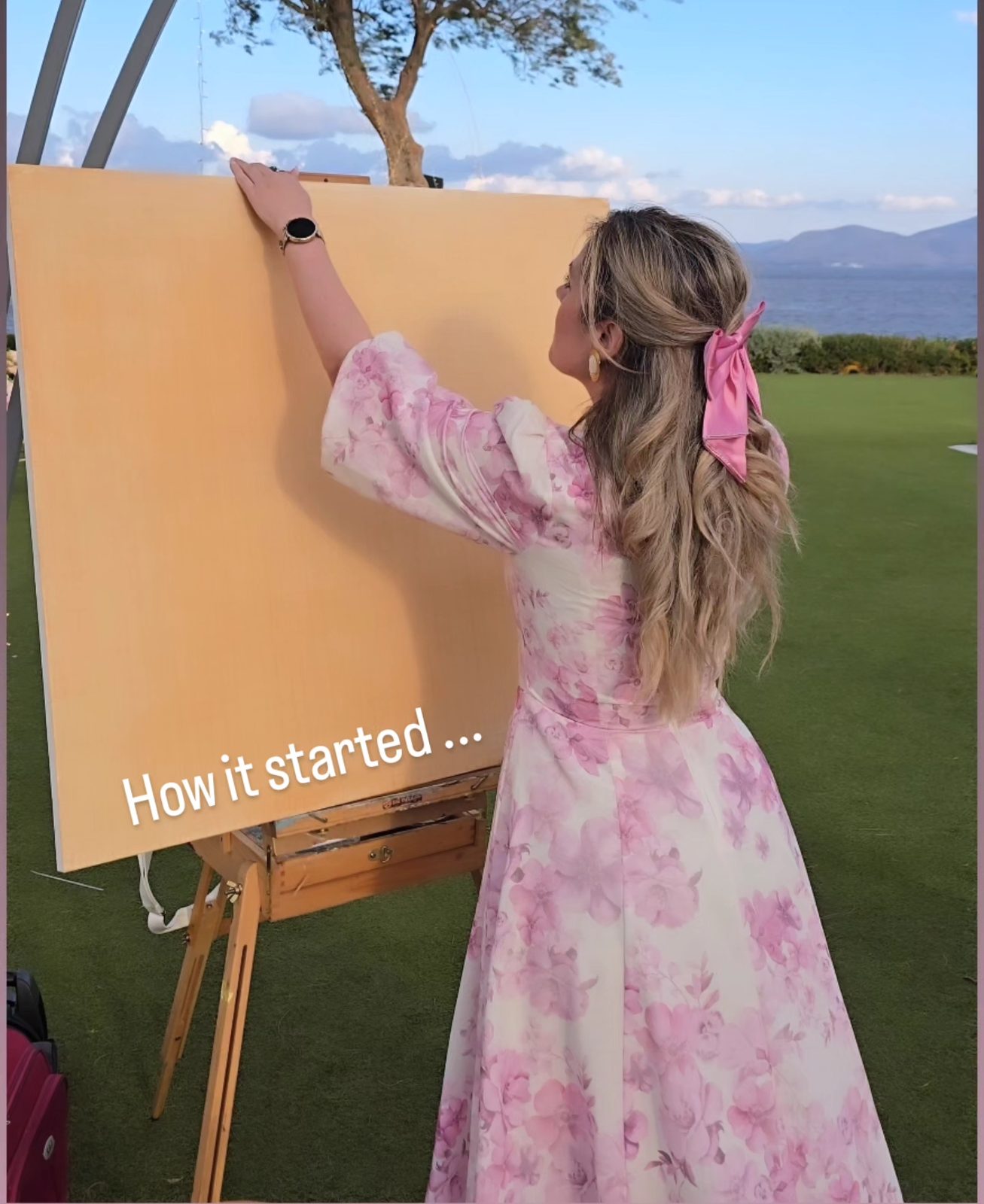 Angela Yfantidou preparing a large blank canvas on the lawn at Island, Athens Riviera, with the sea behind her