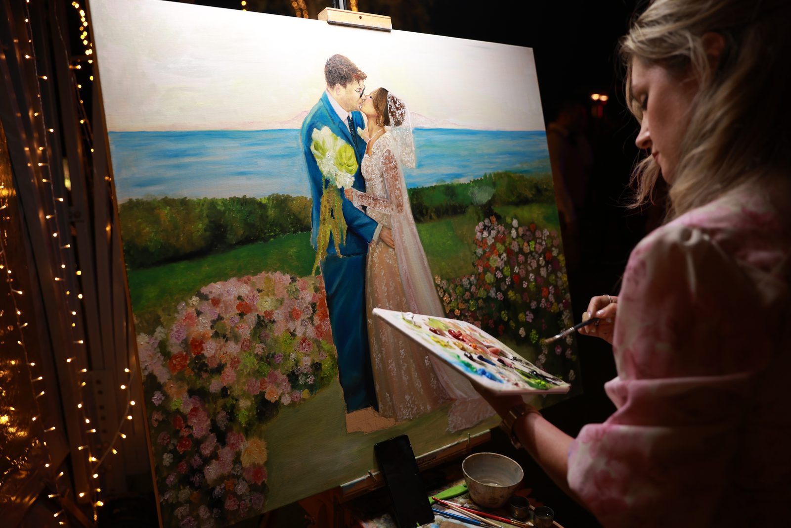 Live wedding painter Angela Yfantidou painting Giannis and Alexandria's large canvas under string lights at Island, Athens Riviera