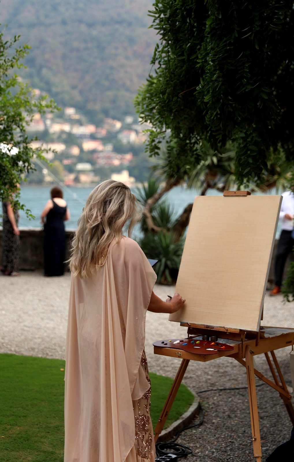Lake Como wedding painter Angela Yfantidou at a blank canvas in the gardens of Villa Pizzo, with Lake Como and the hills of Cernobbio behind