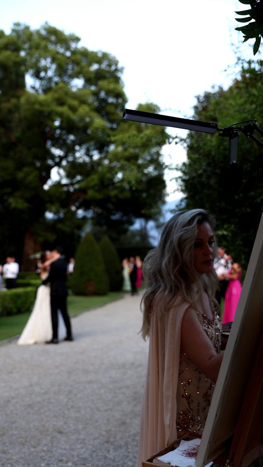Scott and Sydney sharing a moment in the gardens of Villa Pizzo while Angela Yfantidou paints their live wedding portrait in the foreground